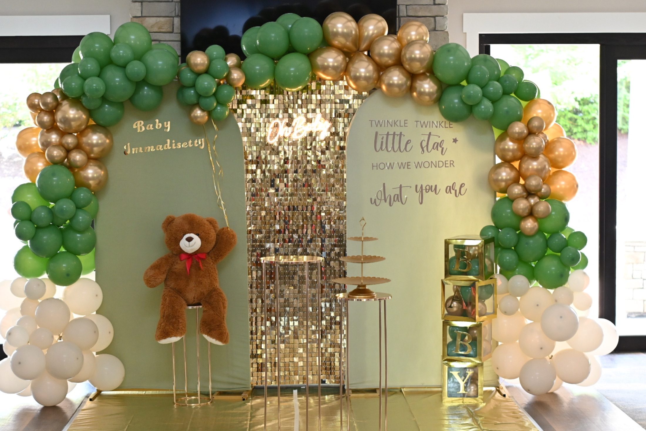 Green, gold, and white baby shower balloon display with a teddy bear